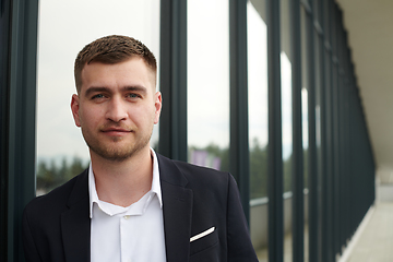 Image showing A CEO dressed in a sleek black suit stands confidently at the entrance of a modern corporate building, awaiting the start of the workday in the bustling urban environment.