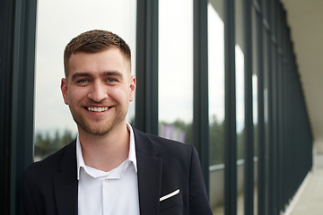 Image showing A CEO dressed in a sleek black suit stands confidently at the entrance of a modern corporate building, awaiting the start of the workday in the bustling urban environment.