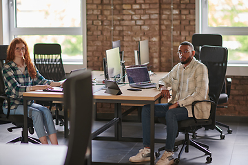 Image showing Group of colleagues, a woman with vibrant orange hair and a young African American businessman, sitting in a modern office space, symbolizing diverse collaboration and a dynamic work environment.