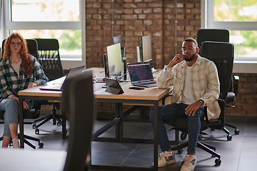 Image showing Group of colleagues, a woman with vibrant orange hair and a young African American businessman, sitting in a modern office space, symbolizing diverse collaboration and a dynamic work environment.