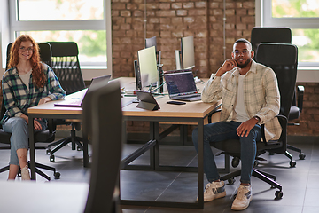 Image showing Group of colleagues, a woman with vibrant orange hair and a young African American businessman, sitting in a modern office space, symbolizing diverse collaboration and a dynamic work environment.