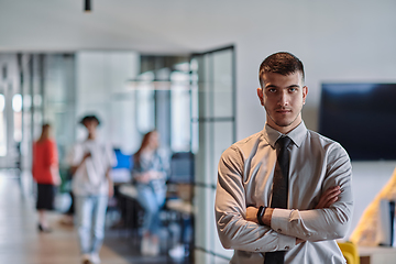 Image showing A young business leader stands with crossed arms in a modern office hallway, radiating confidence and a sense of purpose, embodying a dynamic and inspirational presence.