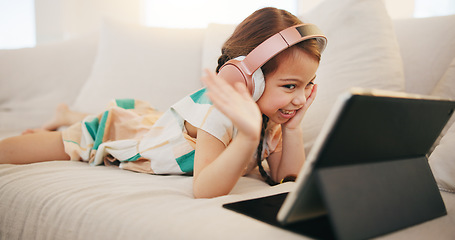 Image showing Happy girl, tablet and headphones on sofa for video call, elearning or streaming at home. Female child or kid smile and wave with technology in relax for virtual class, education or learning at house
