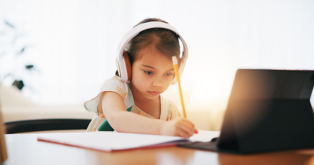 Image showing Girl, headphones and writing in book for elearning, education or study on desk at home. Female person, child or kid taking notes with tablet, headset or technology for virtual class at house