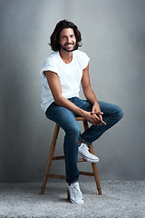 Image showing Fashion, smile and portrait of man in studio on a stool with casual, cool and stylish outfit. Happy, handsome and confident young male model from Mexico with trendy style on chair by gray background.