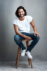 Image showing Fashion, happy and portrait of man in studio on a stool with casual, cool and stylish outfit. Smile, handsome and confident young male model from Mexico with trendy style on chair by gray background.