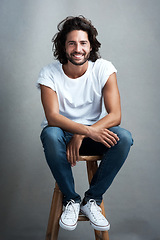 Image showing Fashion, smile and portrait of man in studio on a stool with casual, cool and stylish outfit. Happy, handsome and confident young male model from Mexico with trendy style on chair by gray background.