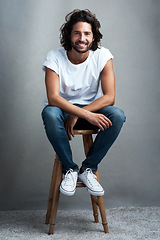 Image showing Fashion, smile and portrait of man in studio on a stool with casual, cool and stylish outfit. Happy, handsome and confident young male model from Mexico with trendy style on chair by gray background.