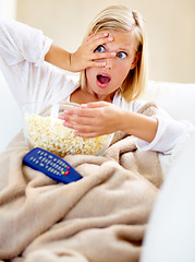 Image showing Horror, popcorn and woman on couch watching tv with remote, blanket and streaming movies in home. Terror, television and girl on sofa in living room with fear for scary video, film or network show.