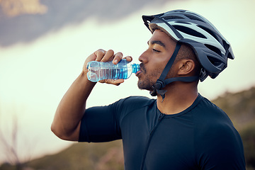 Image showing Fitness man, cycling and drinking water bottle and wearing safety helmet outdoors in nature during summer. Male athlete, exercise and hydration riding a bike to practice, workout or train for sports