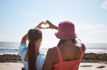 Image showing Beach, heart sign and women friends with love for summer and ocean on blue sky and sunshine. Behind of lesbian couple or gen z people with care hands, icon or emoji for outdoor vitamin d or earth day