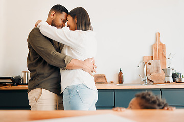 Image showing Cosy couple hugging, romance and affection in a modern kitchen with small child looking at them. Loving, young and parents, mom and dad embrace, excited by the future of their growing family