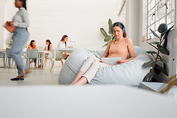 Image showing Serious, young design student relaxing and reading or listening to music in break room in startup office, with colleagues. Modern creative designer working on tablet in casual informal business