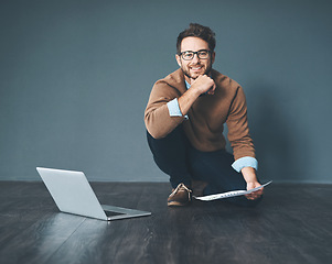 Image showing Happy business man working on laptop, doing tax paperwork and going through finance document while sitting on floor in an office at work. Portrait of entrepreneur planning and completing a project