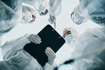 Image showing Hazmat healthcare workers from below, working together during covid pandemic wearing face masks. Team of doctors wearing quarantine suits discussing medical lab results of the virus spread