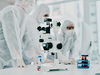 Image showing Sterile, white and modern room with a closeup of a microscope and medical scientists or group conducting research for corona. Clinical and bright laboratory with doctors working on a blood sample.