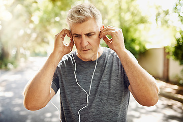 Image showing Fit, mature and healthy or sporty athlete resting after morning run, listening to music outdoors with earphones. Male jogger about to exercise or do cardio training workout for wellness lifestyle.