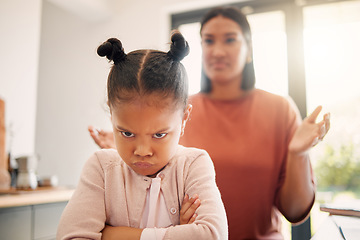 Image showing Angry little girl, unhappy and upset after fight or being scolded by mother, frowning with attitude and arms crossed. Naughty child looking offended with stressed single parent in background.