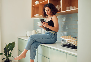 Image showing Afro woman on phone typing, texting or reading online fake news at home drinking coffee or tea. Trendy, young and stylish female sitting on kitchen counter browsing the internet and social media.
