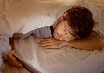 Image showing Man relaxing in bed on a digital tablet browsing on social media or networking on the internet. Male addicted to technology scrolling on mobile at night in a room. Guy searching the web with an ipad.