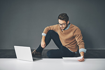 Image showing Business man working on a laptop, reading a report and going through finance paperwork while sitting on the floor in an office at work. Serious professional manager looking at papers with copyspace