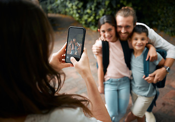 Image showing Mother taking a family photo on her phone of her happy little children and their father smiling before school. Boy and girl siblings with their dad smile for a picture. Mom taking photos of kids