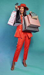 Image showing Shopping with credit card, holding bags and enjoying retail therapy spree while standing against a blue studio background. Stylish, elegant and beautiful woman buying items and fashion clothes