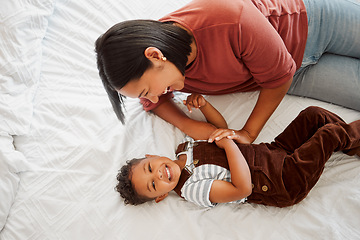 Image showing Playful, fun and funny mother playing and bonding with her son laughing together on a bed at home from above. A single mom enjoying quality time and parenting her child or kid in the bedroom