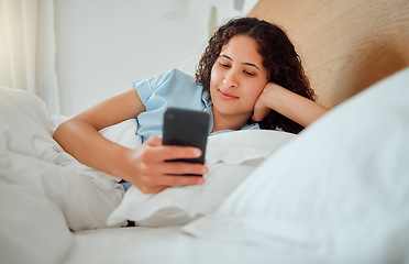 Image showing Woman texting, checking messages and holding phone while reading sms and lying awake in her bed in the morning. Happy, content and smiling female playing a game, browsing the internet or social media