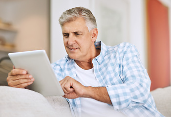 Image showing Mature and senior man browsing on tablet, searching the internet and scrolling on social media while sitting on the couch at home. One retired male reading, checking and replying to messages online