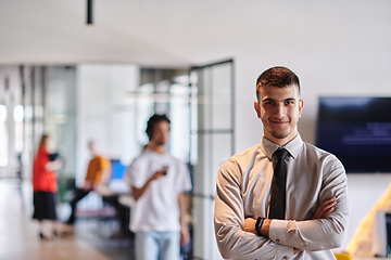 Image showing A young business leader stands with crossed arms in a modern office hallway, radiating confidence and a sense of purpose, embodying a dynamic and inspirational presence.