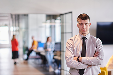 Image showing A young business leader stands with crossed arms in a modern office hallway, radiating confidence and a sense of purpose, embodying a dynamic and inspirational presence.