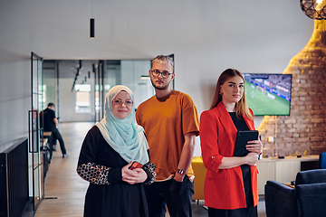 Image showing A group of young business colleagues, including a woman in a hijab, stands united in the modern corridor of a spacious startup coworking center, representing diversity and collaborative spirit.