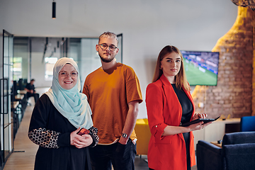 Image showing A group of young business colleagues, including a woman in a hijab, stands united in the modern corridor of a spacious startup coworking center, representing diversity and collaborative spirit.