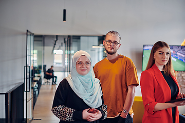 Image showing A group of young business colleagues, including a woman in a hijab, stands united in the modern corridor of a spacious startup coworking center, representing diversity and collaborative spirit.