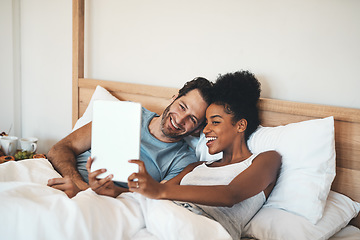 Image showing Happy couple taking selfie on a tablet in bed together after waking up. Interracial husband and wife enjoying their relationship, having fun while bonding and relaxing indoors on a weekend