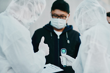 Image showing Negative covid test and thumbs up for young man from healthcare worker after testing for virus. Medical professionals in hazmat suits taking temperature tests during disease outbreak or pandemic