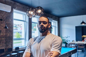 Image showing An African American businessman posing with crossed arms, exuding confidence and empowerment within the modern business setting of a startup coworking center.