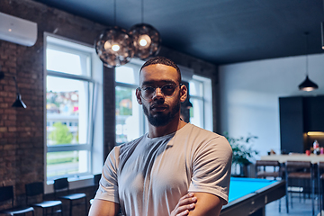 Image showing An African American businessman posing with crossed arms, exuding confidence and empowerment within the modern business setting of a startup coworking center.