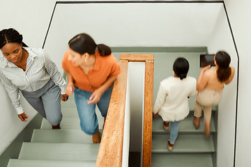 Image showing Overhead of busy, diverse female colleagues returning to work after break, with blurred digital tablet screen. Active business woman in motion talking and walking up office building stairs.