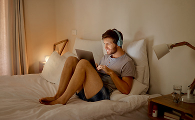 Image showing Laptop, internet and relax with a young man streaming music, video or a podcast online with technology and sitting on his bed in the bedroom at home. Enjoying freedom, tech and radio during free time