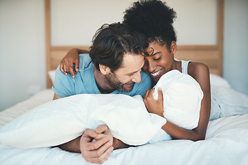 Image showing Fun interracial couple laughing, bonding and lying on bed in a home bedroom and looking happy, in love and playful. Smiling man and woman hugging and cuddling after waking up in the morning together