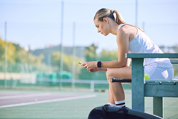 Image showing Fit tennis player with phone checking fitness goal progress on a sports exercise app online while taking a break at the court. A sportswoman checking messages on cellphone and waiting for a coach