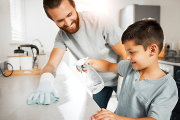 Image showing Father teaching young son cleaning chores in the family home having fun and bonding together. Smiling and loving father helping, washing and wiping kitchen counter with his little boy indoors