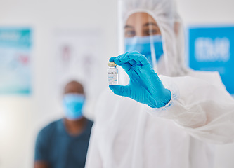 Image showing Covid vaccine, cure or treatment for covid19 held by a healthcare professional in a hospital. Portrait of a doctor wearing a protective hazmat suit holding a bottle of medicine in a clinic, hospital