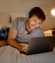Image showing Typing, headphones and in bed on laptop young man looking for movie or video to watch and relax at night in home. Happy male on internet and listening to music on streaming website and social media