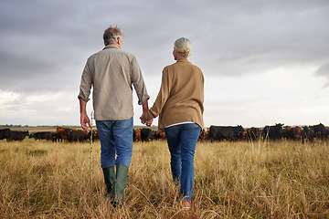 Image showing Mature couple holding hands and walking on a cattle farm, bonding and having a stress free day together. Senior farmers enjoying outdoors, being active and loving on romantic walk at sunset