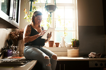 Image showing Trendy woman browsing internet on tablet using her new wifi at home looking happy and satisfied. Normal, real and edgy young female searching online for cool recipe ideas to use in her modern kitchen