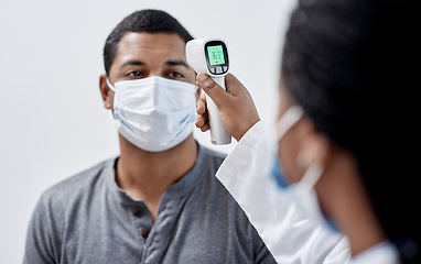 Image showing Male covid patient getting his temperature taken with medical equipment by a doctor in hospital consultation room. Man wearing mask and health care professional pointing digital infrared thermometer.