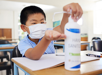 Image showing Hygiene, safety and covid routine of a little boy using hand sanitizer at school. Young asian student with a mask practicing good health by cleaning his hands at his classroom desk in a pandemic